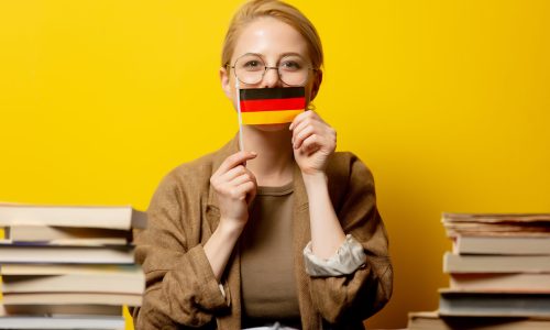 Style blonde woman sitting at table with books and flag of Germany on yellow background