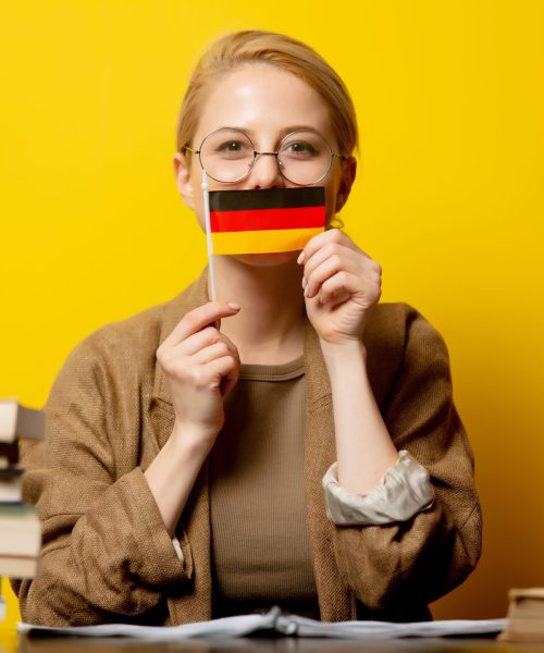 Style blonde woman sitting at table with books and flag of Germany on yellow background
